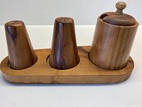 Front view of fitted olive wood tray holding three condiment containers: salt shaker, pepper shaker, lidded jar