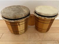 Two connected hand made wooden bongo drums with leather heads, front angled view showing natural wood grain and drum head texture.