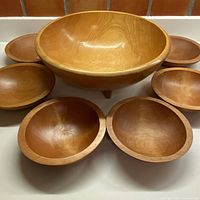 Full view of the large three-legged salad bowl surrounded by six smaller matching bowls on a flat surface, showing overall set appearance and condition.