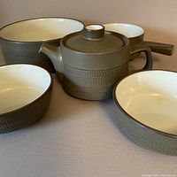 Full set displayed including large serving bowl, teapot, gravy boat, and dessert bowls showing olive green color and chevron texture.