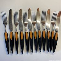 Top view of 6 steak knives and 6 forks with black and melon bakelite handles arranged in alternating order