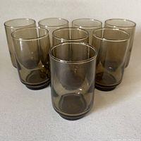 Front angle of 8 smoky brown shot glasses arranged in a loose cluster on white surface