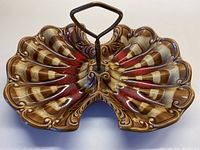 Top-down view of the ceramic bowl showing shell-like ridges, multicolor glaze pattern, and metal handle in the center.