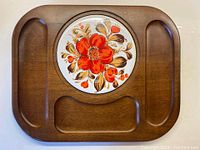 Full top view of solid wood cheeseboard with circular colorful ceramic tile with floral design in the center and three carved serving indents around it.