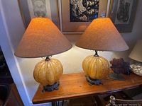 Pair of amber convex blown glass lamps with beige textured lampshades placed on a wooden table, showing overall size and style.