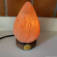 Front angle view of the glowing Himalayan salt lamp shaped like a pinecone sitting on a wooden base with a yellow circular design.