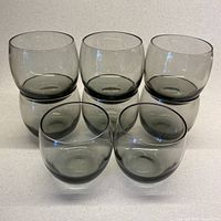 Set of 8 smoky grey lowball glasses arranged in a group, showing the chubby round shape and consistent color tone.