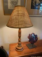 Vintage hand turned wooden lamp with burlap shade on a wooden table, lit to show lighting effect.