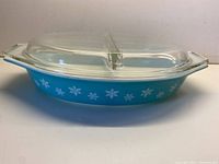 Side view of blue Pyrex casserole with white snowflake pattern and clear divided lid in place.