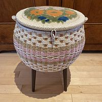 Front view of the woven sewing basket on wooden legs, showing the body weave and legs.