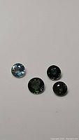 Four round faceted sapphires in varying shades of blue to green from sellers personal collection on white background