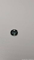Oval cut blue-green sapphire gemstone on white background, showing color and facets.