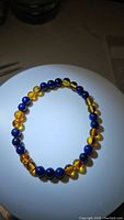 Top-down view of amber and lapis lazuli beaded stretchy bracelet on white surface with light spot, showing translucent amber beads and deep blue lapis beads alternating evenly.