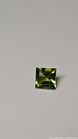 Photo showing the square cut apple green Peridot gemstone with good clarity on a plain white background.