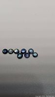 Seven round blue sapphire cabochons laid out on white background, showing glossy blue hues and varying shades of blue in the stones.