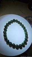 Photo of round polished dark green jade beads stretchy bracelet on white background shows color and bead detail.