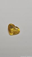 Heart-shaped natural canary yellow sapphire on a plain background, showing facets and internal inclusions.