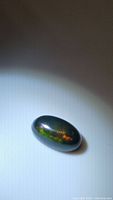 Oval cabochon black Ethiopian opal on flat surface showing rainbow flashes under light.