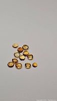 Fourteen small to medium round yellow-orange citrine cabochon gemstones arranged on white background, showing color and cut clearly.