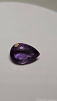 Close-up photo of deep purple pear-shaped faceted amethyst gemstone with good transparency and no visible inclusions.
