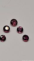 Five round cut deep hot pink to purple sapphire gemstones displayed on neutral background.