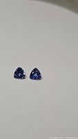 Two deep blue-purple trillion cut tanzanite gemstones shown side by side on a plain white background.