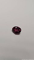 Photo of bright vivid hot pink purple Rhodolite garnet gemstone in teardrop cut, showing faceted surfaces and color depth.
