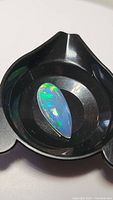Pear-shaped crystal Ethiopian opal cabochon in a black holder, showing vibrant green and blue fire colors with some red flashes.