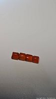 Four square cabochon mandarin orange carnelian gemstones displayed in a row on a plain surface.