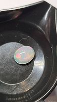 Oval cabochon cut Ethiopian fire opal gem on a black surface showing clear bright play-of-color in natural light.