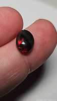 Close-up image of a natural Ethiopian black opal held on a fingertip showing its oval shape, black base color and bright red flashes.