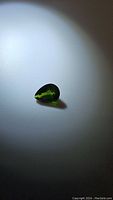 Pear-shaped natural chrome diopside gemstone shown on white background under focused light to highlight color and facets.