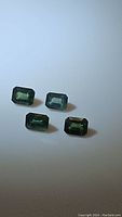 Photo showing four emerald cut blue-green sapphires on white background with clear view of shape, size and color.