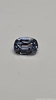 Close-up image of a cushion cut blue sapphire with faceting visible, showing natural internal characteristics and high clarity.