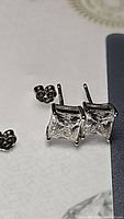 Close-up of both princess cut square moissanite stud earrings, one earring with butterfly backing visible