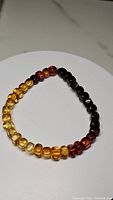 Bracelet showing the gradient pattern of polished Baltic amber beads from light yellow to dark brown, laid flat on a white circular platform.