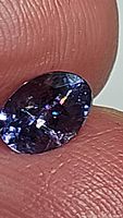 Close-up image showing the oval cut tanzanite held between fingers, highlighting the internal rainbow inclusion inside the gem.