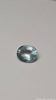 Photograph of the loose oval cut sky blue aquamarine gemstone on a plain background showing color and cut details.