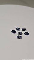 Six oval cut tanzanite gemstones displayed on a light background highlighting their purple-blue color and facets.