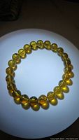 Photo showing the translucent golden-yellow Baltic amber beads strung in a circular bracelet, illuminated to highlight clarity and color.