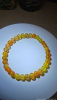 Top view of a stretchy bracelet made of polished yellow and orange agate beads arranged in a circle on a white background.