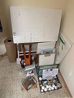 Overview of white drawing table leaning against wall, wooden easel support, stacked canvases and art supply containers, roll of kraft paper