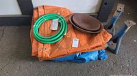 Top-down view of orange tarp, blue tarp underneath, green hose coiled, two brown prospecting pans and part of two blue metal car hoists