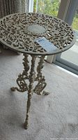 Side view of round cast iron table showing intricate openwork floral design and ornate legs with rust spots.