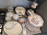 Full lot on countertop showing soup terrine, ladle, matching plates, serving bowl, small bowls, covered dish, ceramic bird figurines, and mugs.