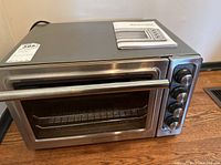 Front angled view of compact KitchenAid oven on wooden surface with manual on top.