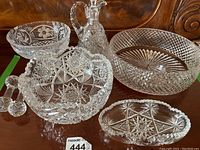 Full set of cut crystal items consisting of decanter, three bowls, spoon rest shown on wooden surface.