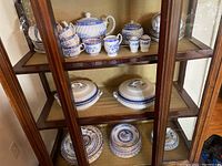 Porcelain tea and dish set displayed in wooden glass cabinet, showing full collection including cups, saucers, covered dishes, and teapot.