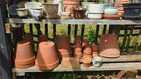 Wide view of multiple gardening pots including terracotta and ceramic, showing various sizes, shapes, and colors arranged on wooden shelves.