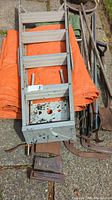 Top view of 5-foot aluminum step ladder lying on orange tarp with ax heads and various gardening tools beside it on stone pavement.